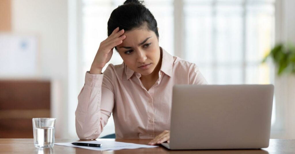 Young woman looking worried at desk with hand on forehead